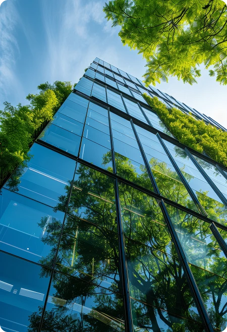 Fachada envidraçada de edifício moderno refletindo árvores e céu azul, representando a integração entre desenvolvimento urbano e sustentabilidade ambiental.